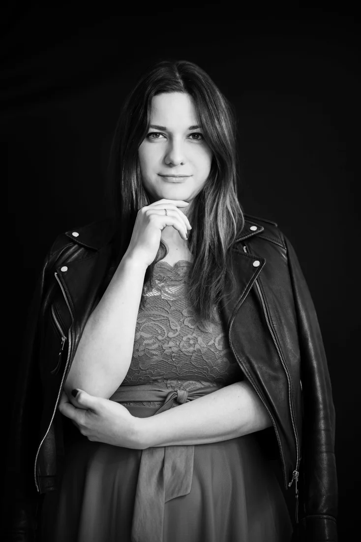 Portrait en noir et blanc d’une femme, main sous le menton et veste en cuir sur les épaules.