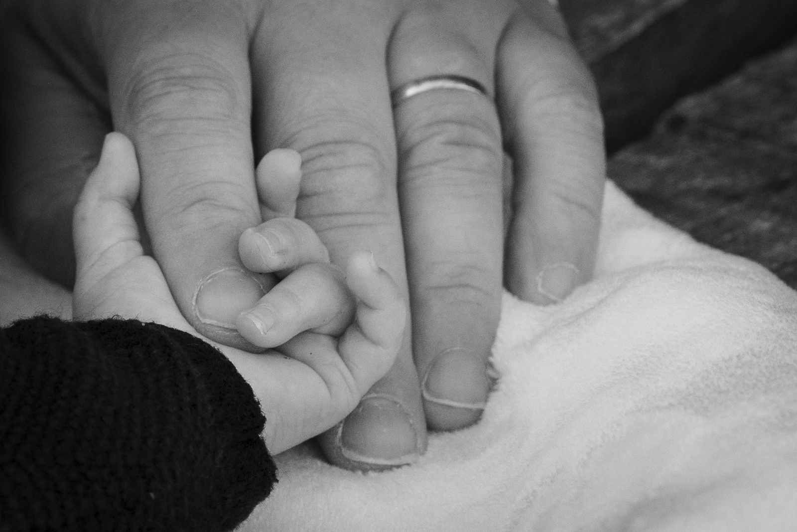 La petite main d’un bébé entoure le doigt d’un adulte, en noir et blanc.